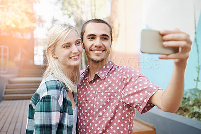 Buy stock photo Shot of a happy young couple using a mobile phone to take selfies outside