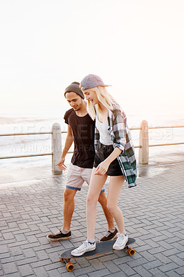 Buy stock photo Couple, man and woman with skateboard on promenade, happy and helping for balance, learning and playful by sea. People, teaching and skating with support and fun on boardwalk for vacation in Italy