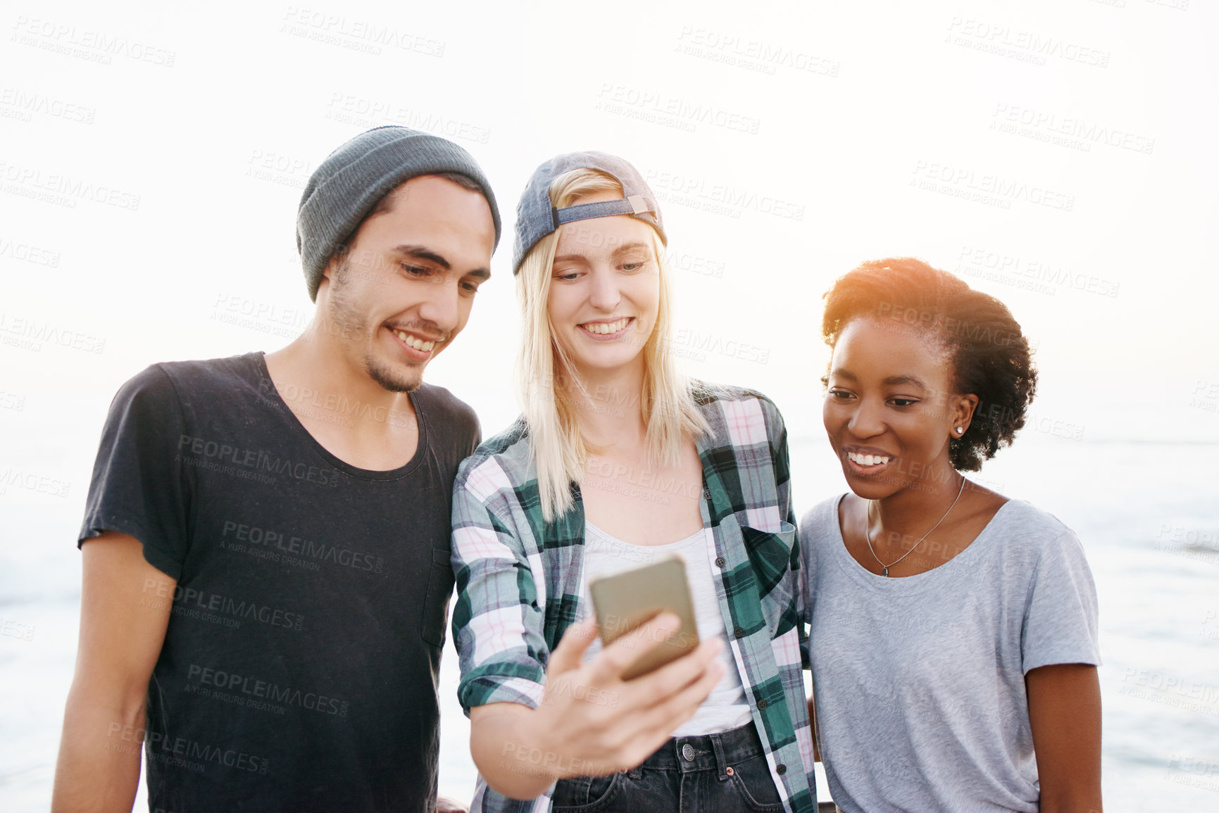 Buy stock photo Cropped shot of a group of friends looking at a cellphone while walking on the promenade