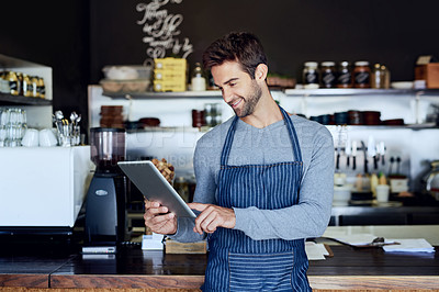 Buy stock photo Cropped shot of a handsome young barista using a tablet in his coffee shop