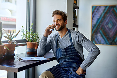 Buy stock photo Cropped shot of a handsome young barista taking a call while working in his coffee shop