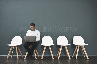 Buy stock photo Shot of a young man using a laptop while waiting in line for a job interview