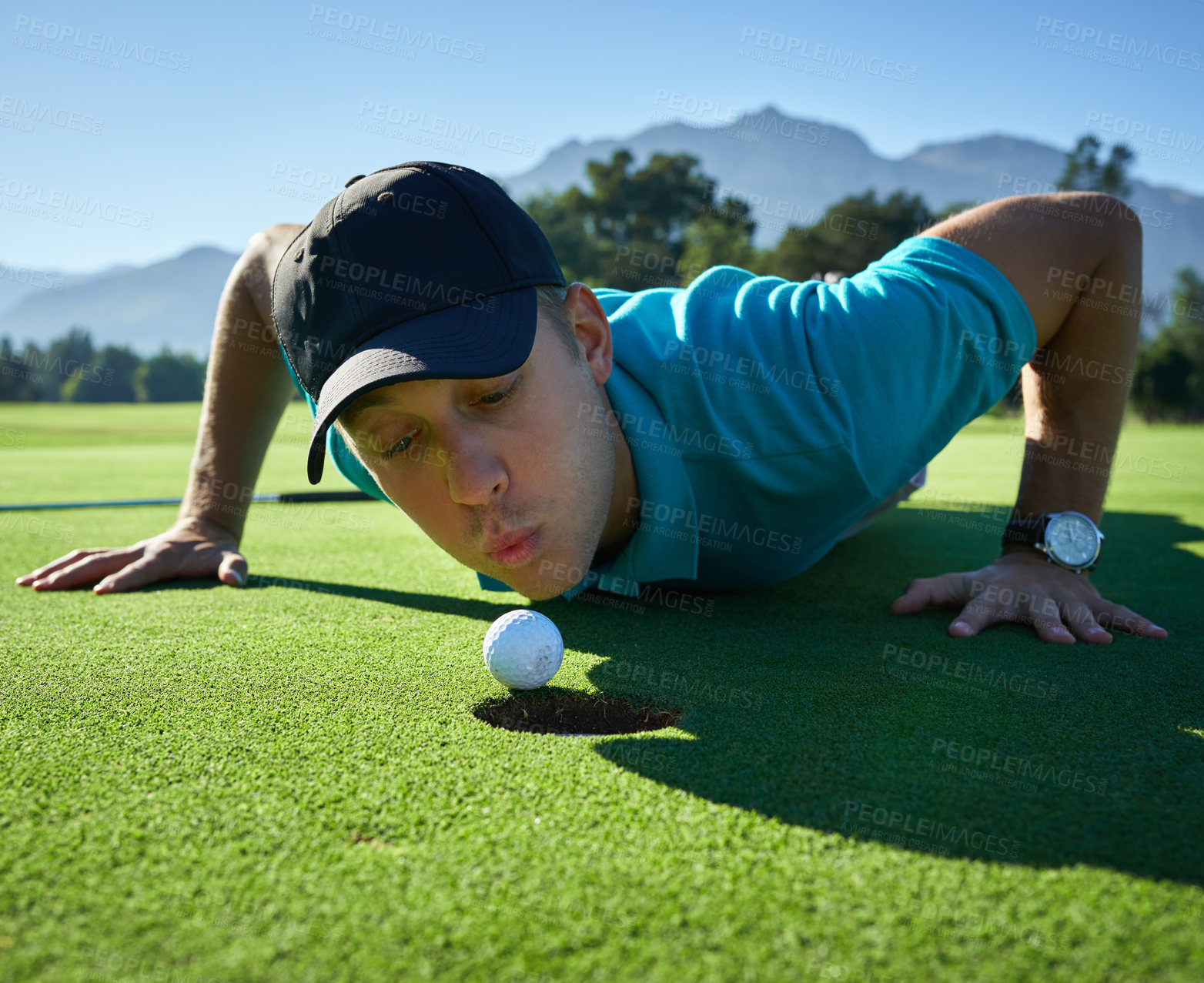 Buy stock photo Low angle shot of a carefree young man blowing a golf ball into a hole on a golf course