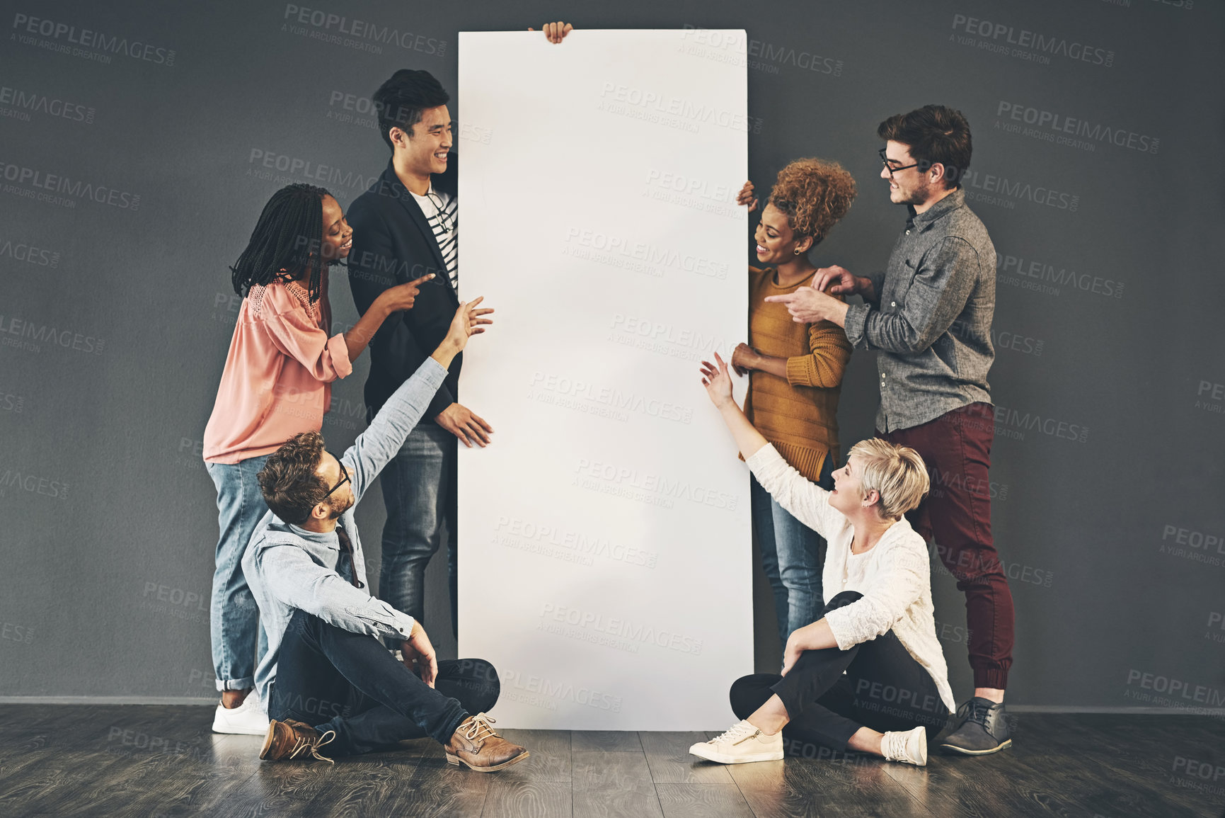 Buy stock photo A diverse group of people holding a blank white board or poster and showing advertising copy space. A team or friends marketing a placard banner standing and sitting together for a promotion