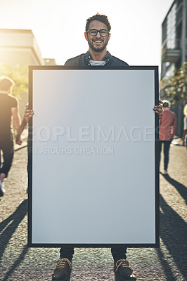 Buy stock photo Young man holding an empty sign, board or placard while standing outside in the city street. Portrait of one happy, smiling and cheerful guy making an announcement, showing a poster for promotion