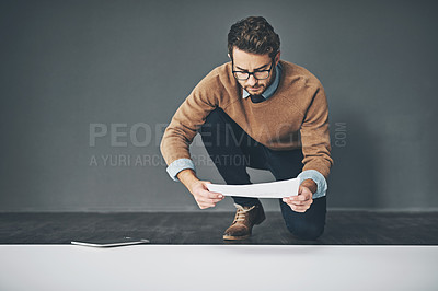 Buy stock photo Studio shot of a young businessman looking through paperwork against a grey background