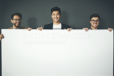 Buy stock photo A group of young, smiling and professional business men holding a white sign copyspace portrait. A team of male designers standing together with a blank billboard for advertising or marketing
