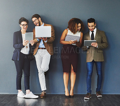 Buy stock photo Happy workers using digital devices standing together on a work break. Group of relaxed employees using technology, a phone, computer and tablet. Office business team enjoying social media indoors