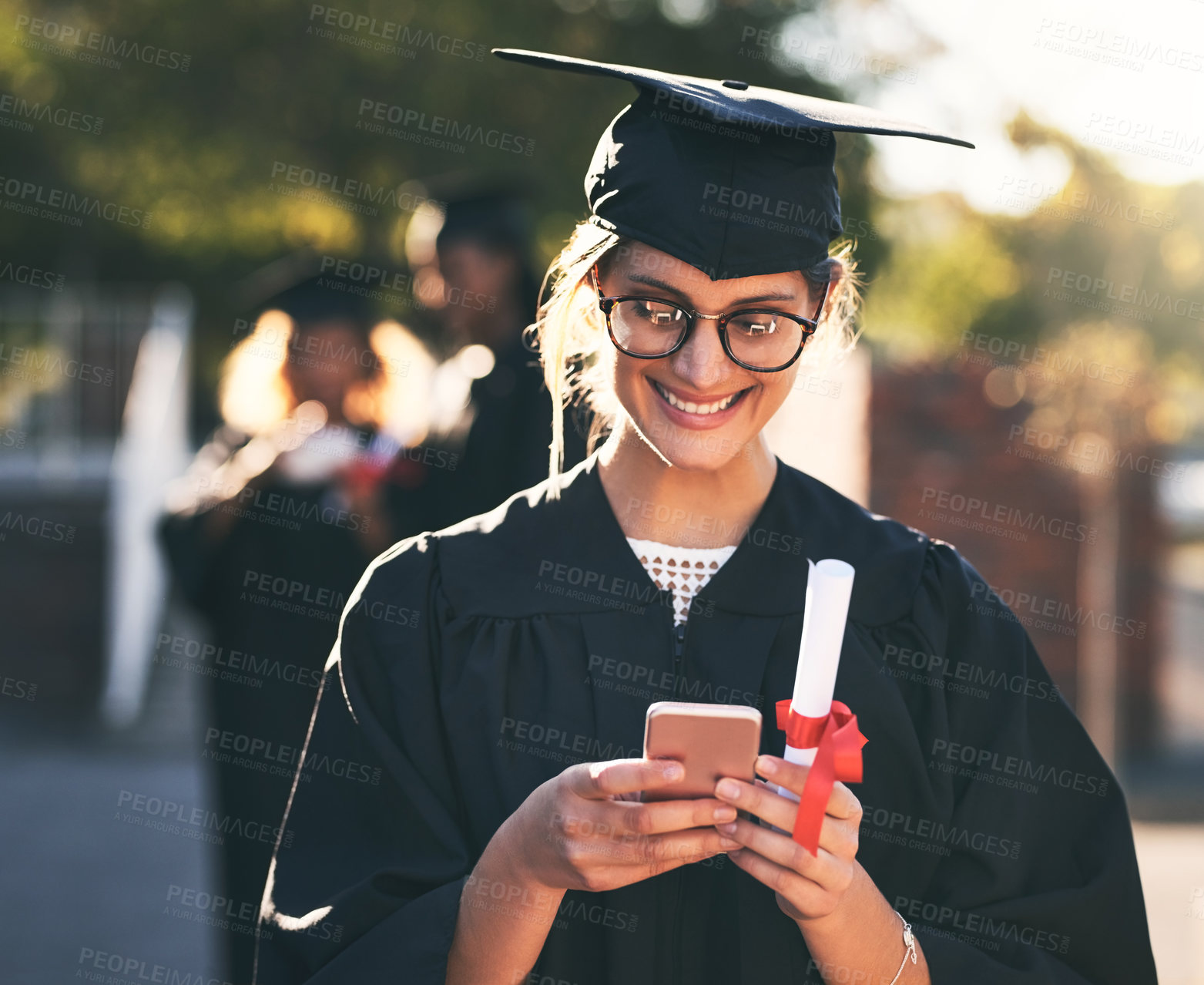 Buy stock photo Shot of a young woman using a mobile phone on graduation day