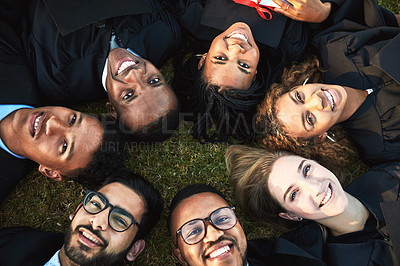 Buy stock photo High angle shot of a group of students relaxing on the grass together on graduation day