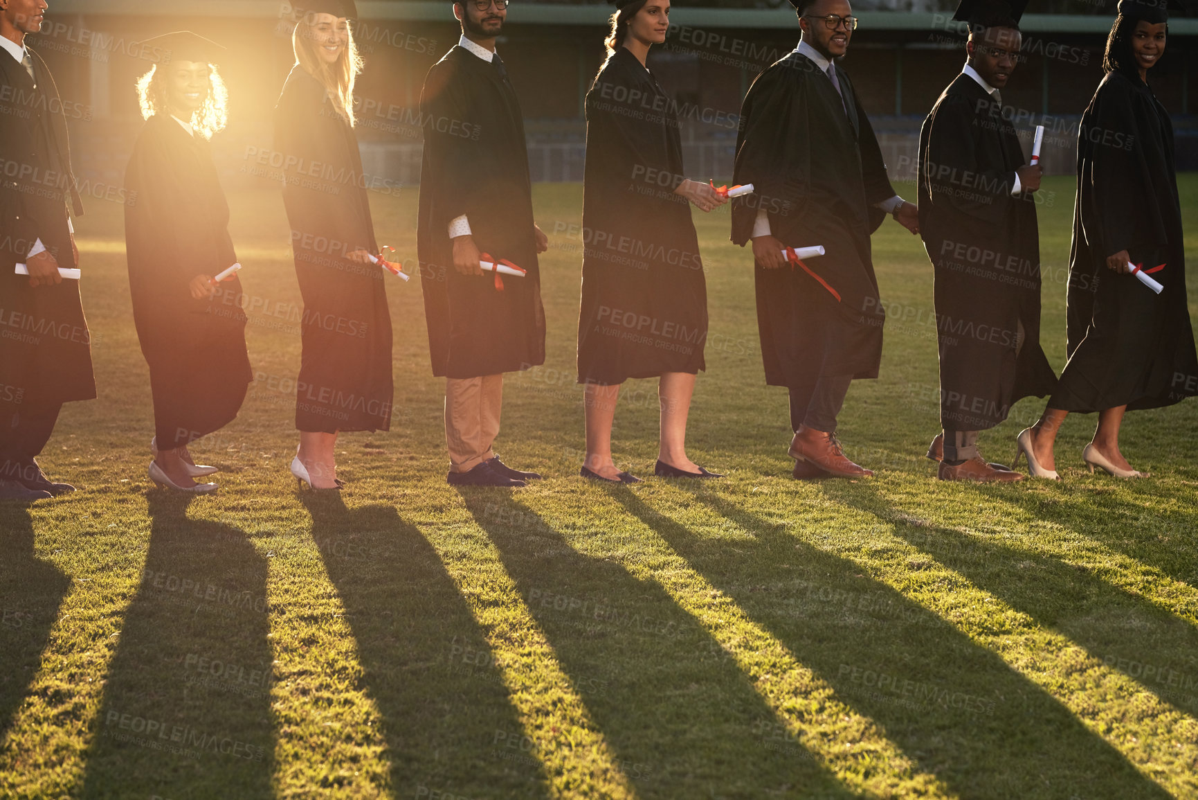 Buy stock photo Row, group and graduation of students, outdoor and together with degree, achievement and happy in school. University, lens flare and qualification in academy, celebration and shadow of people