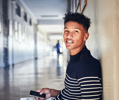 Buy stock photo Cropped portrait of a handsome young male student using his cellphone while sitting in the university corridor between classes
