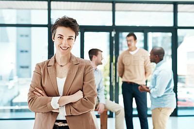 Buy stock photo Portrait of a designer standing with her arms crossed with colleagues blurred in the background