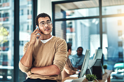 Buy stock photo Shot of a designer talking on his phone with his colleagues blurred in the background