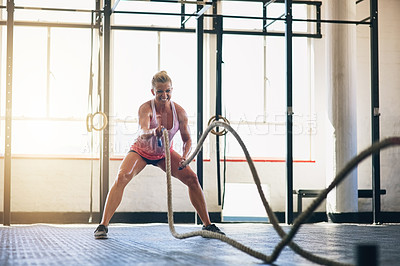 Buy stock photo Shot of a sporty young woman working out with heavy ropes at the gym