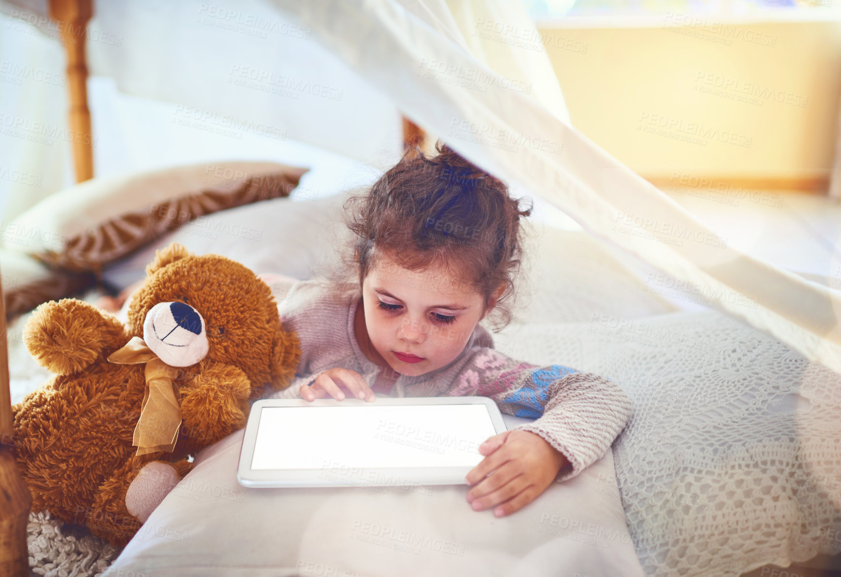 Buy stock photo Tent, relax and child on tablet in home for watching movies, online games and streaming cartoons. Family, mockup screen and young girl with teddy bear on digital tech for internet videos in bedroom