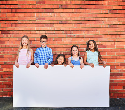 Buy stock photo Portrait of a group of young children holding a blank sign against a brick wall