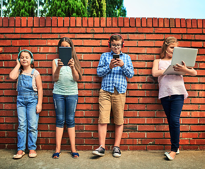 Buy stock photo Shot of a group of young children using digital devices against a brick wall