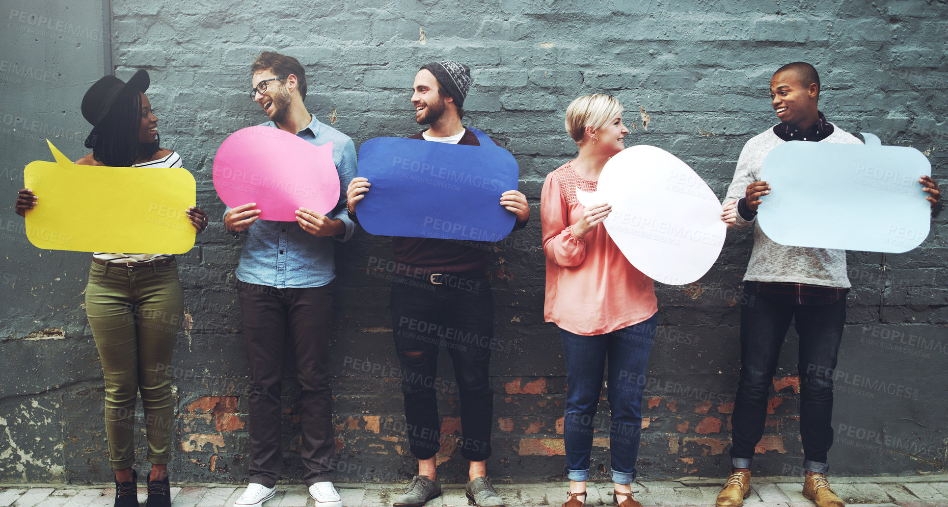 Buy stock photo Shot of a diverse group of people holding up speech bubbles against a gray brick wall