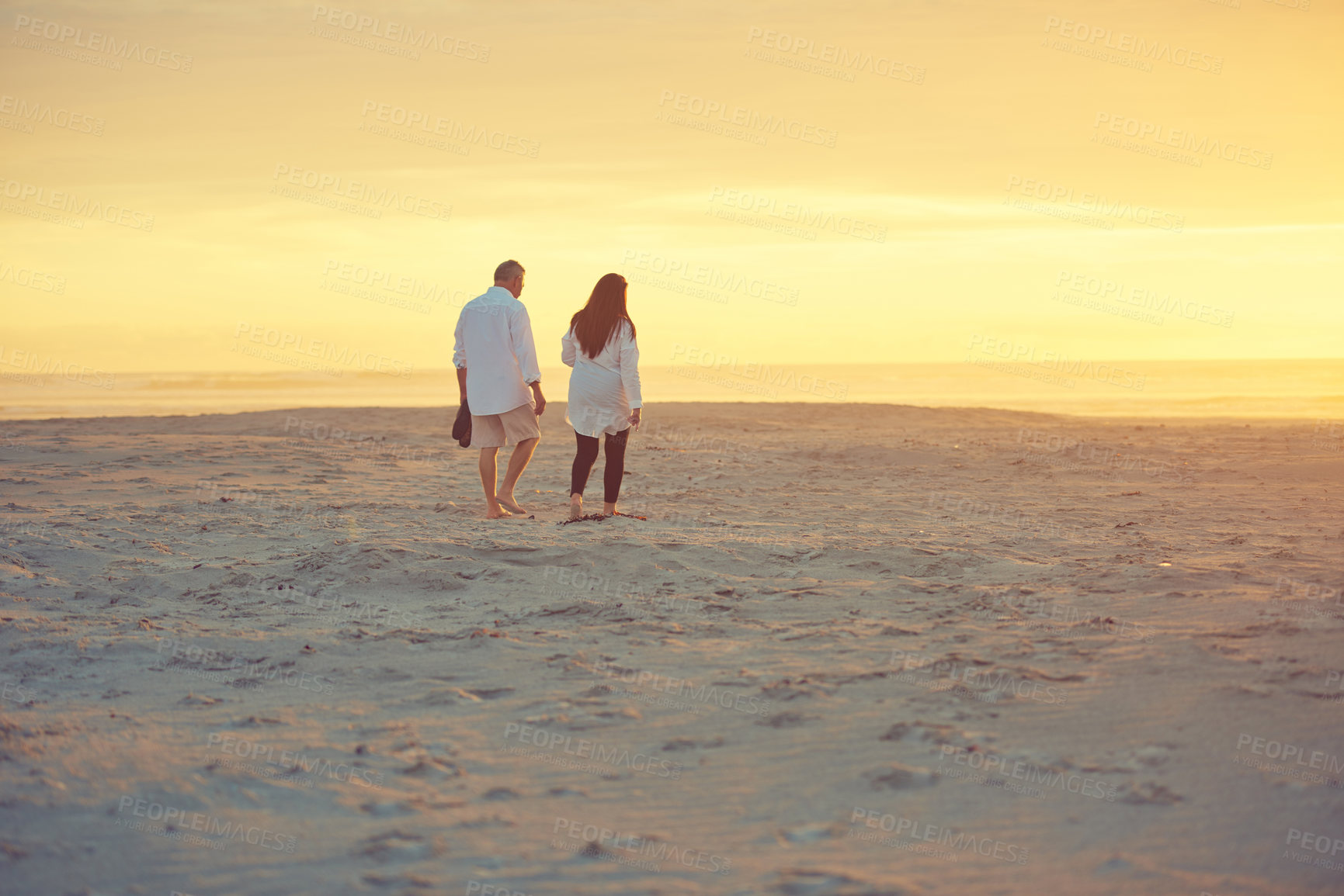 Buy stock photo Rearview shot of an affectionate mature couple walking on the beach