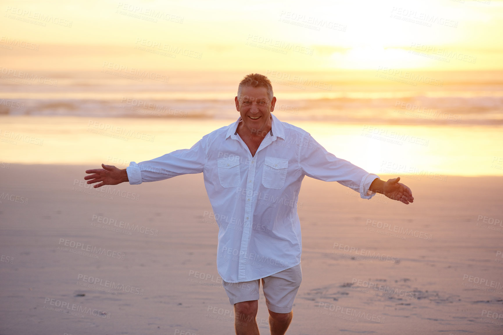 Buy stock photo Cropped portrait of a handsome mature man standing with his arms outstretched on the beach at sunset