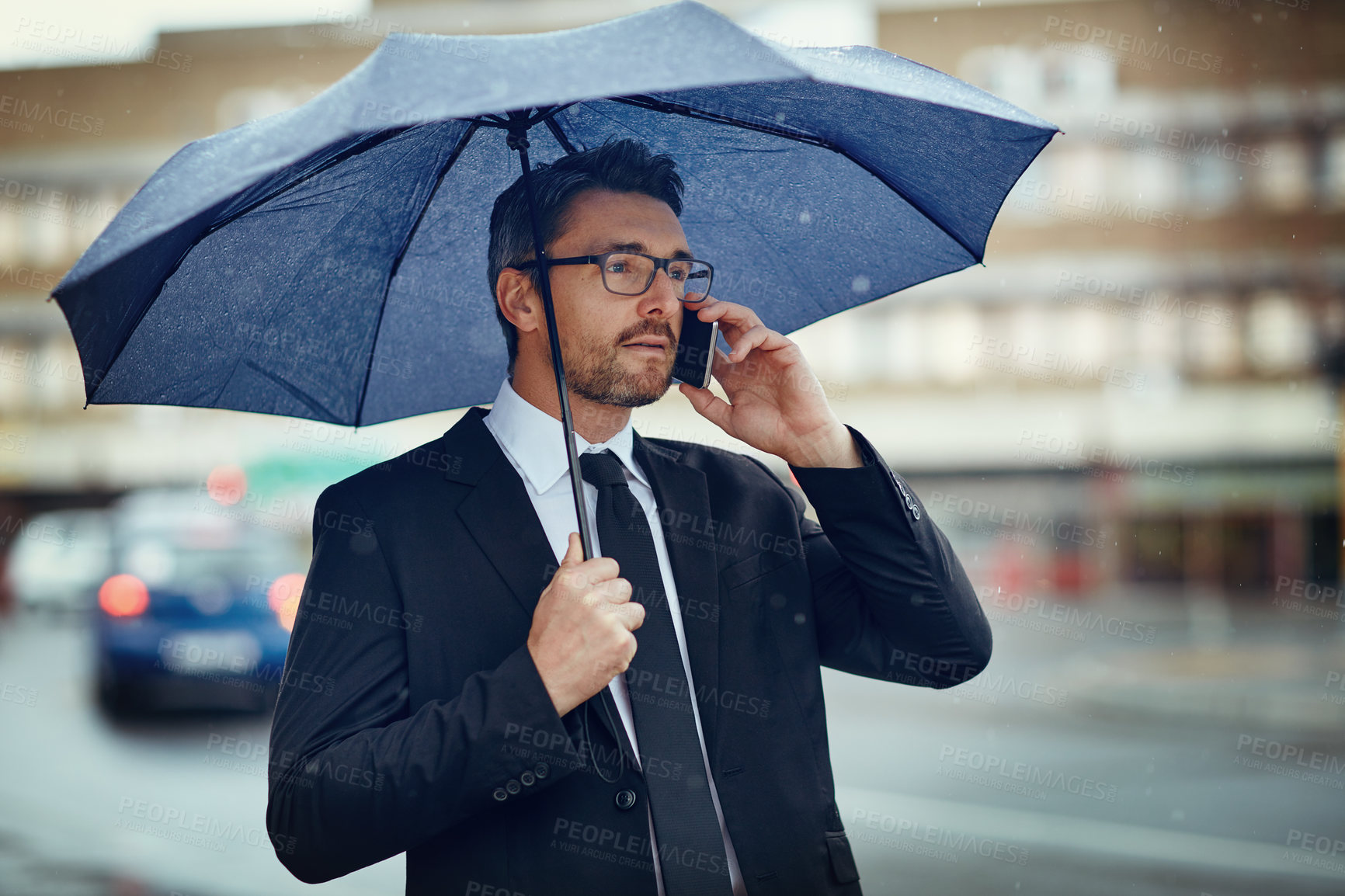 Buy stock photo Shot of a mature businessman talking on a cellphone and holding an umbrella while out in the city