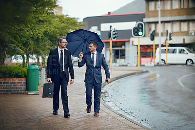 Buy stock photo Shot of two corporate businessmen travelling through the city on a rainy day