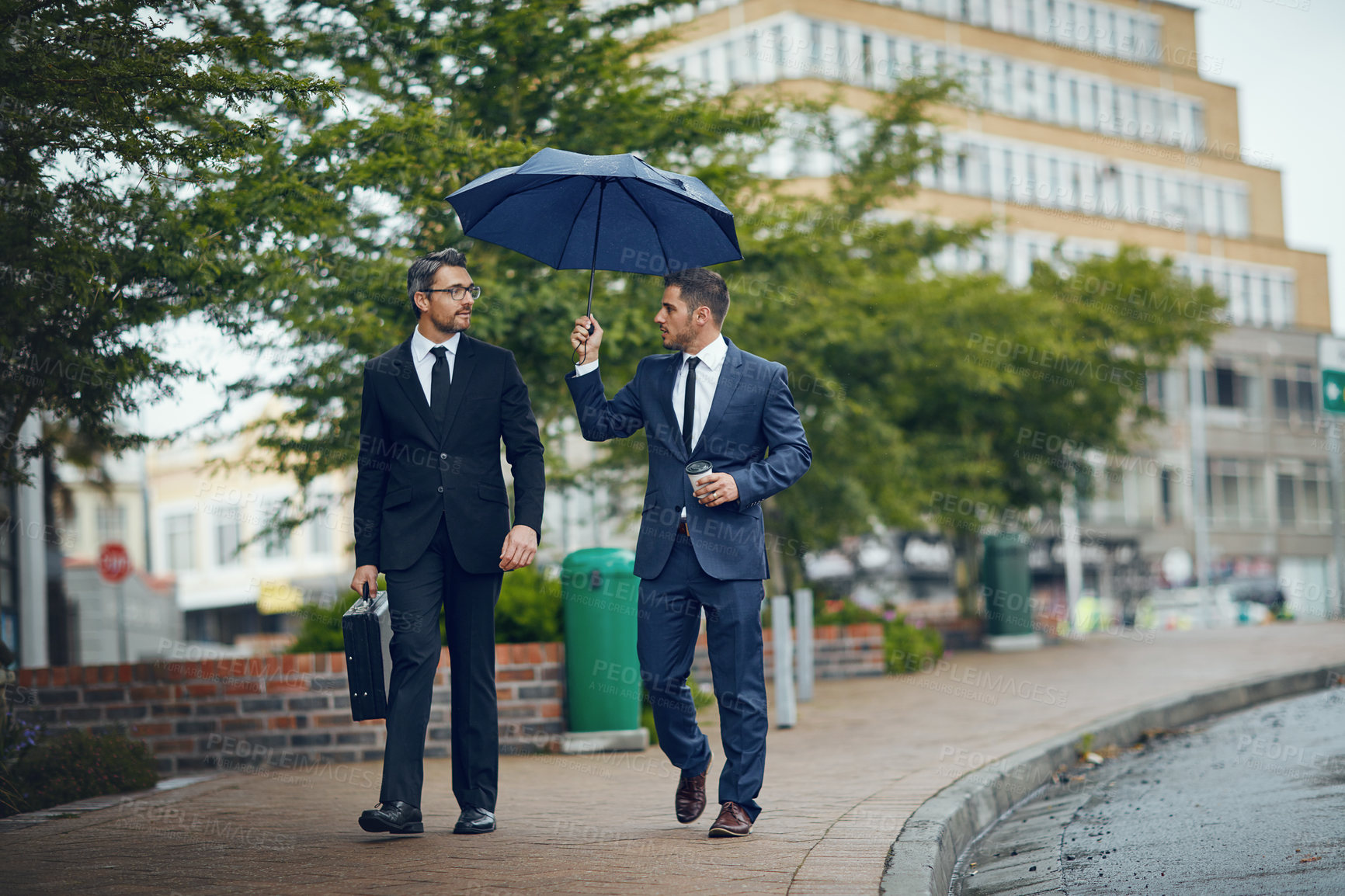 Buy stock photo Shot of two corporate businessmen travelling through the city on a rainy day