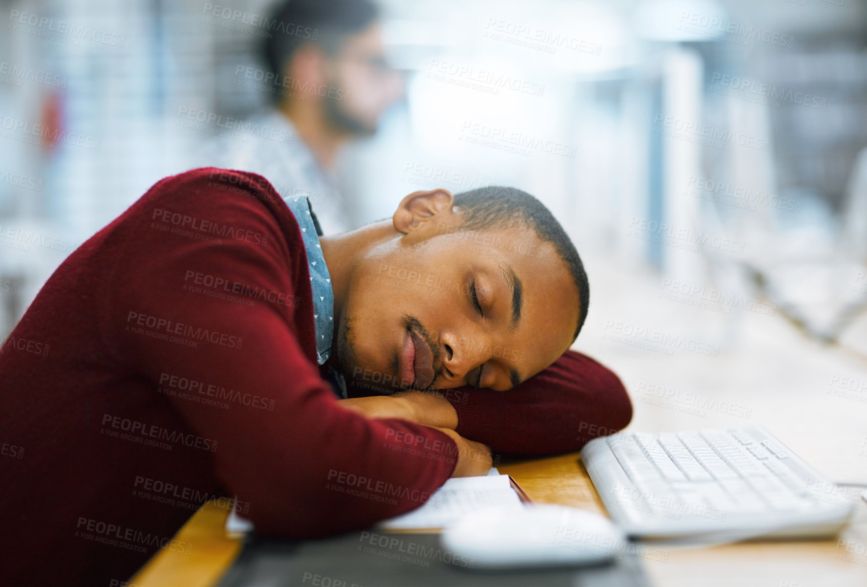 Buy stock photo Shot of a tired young man sleeping on a desk with his arms folded inside of a library