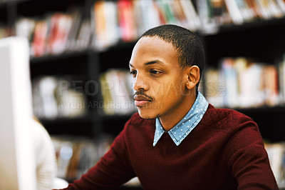 Buy stock photo Shot of a focused young man working on a computer while being seated in a library