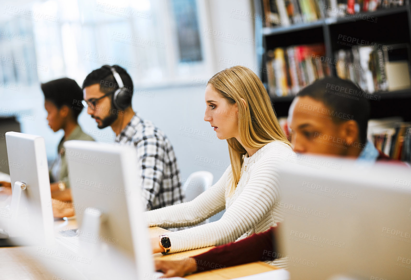 Buy stock photo Shot of a group young students working on computers and making notes in a library