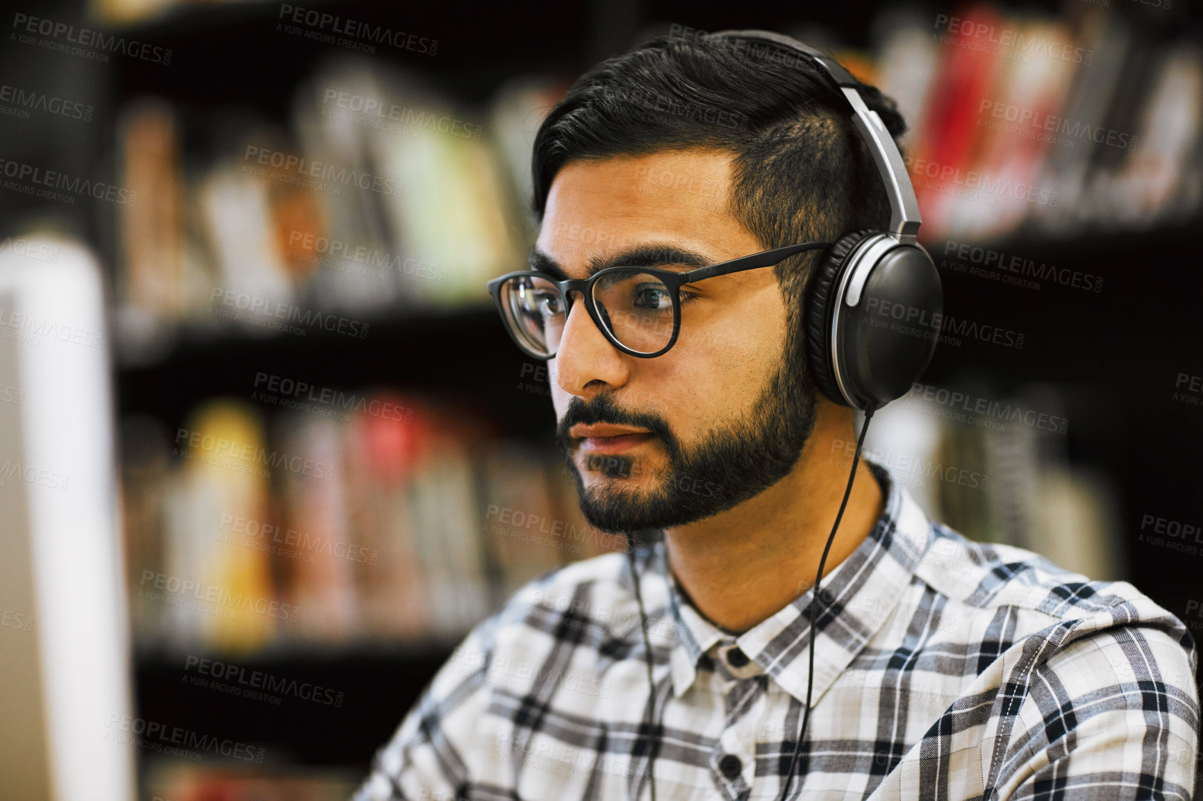 Buy stock photo Closeup shot of a focused young man sitting and working on a computer in a library while listening to music