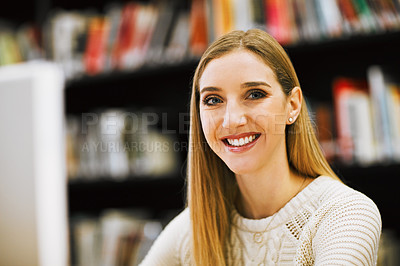 Buy stock photo Shot of a cheerful young woman working on a computer while being seated in a library and looking at the camera