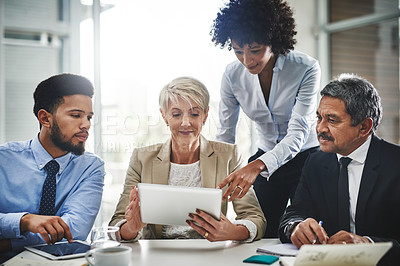 Buy stock photo Shot of a group of businesspeople discussing something on a digital tablet in a meeting