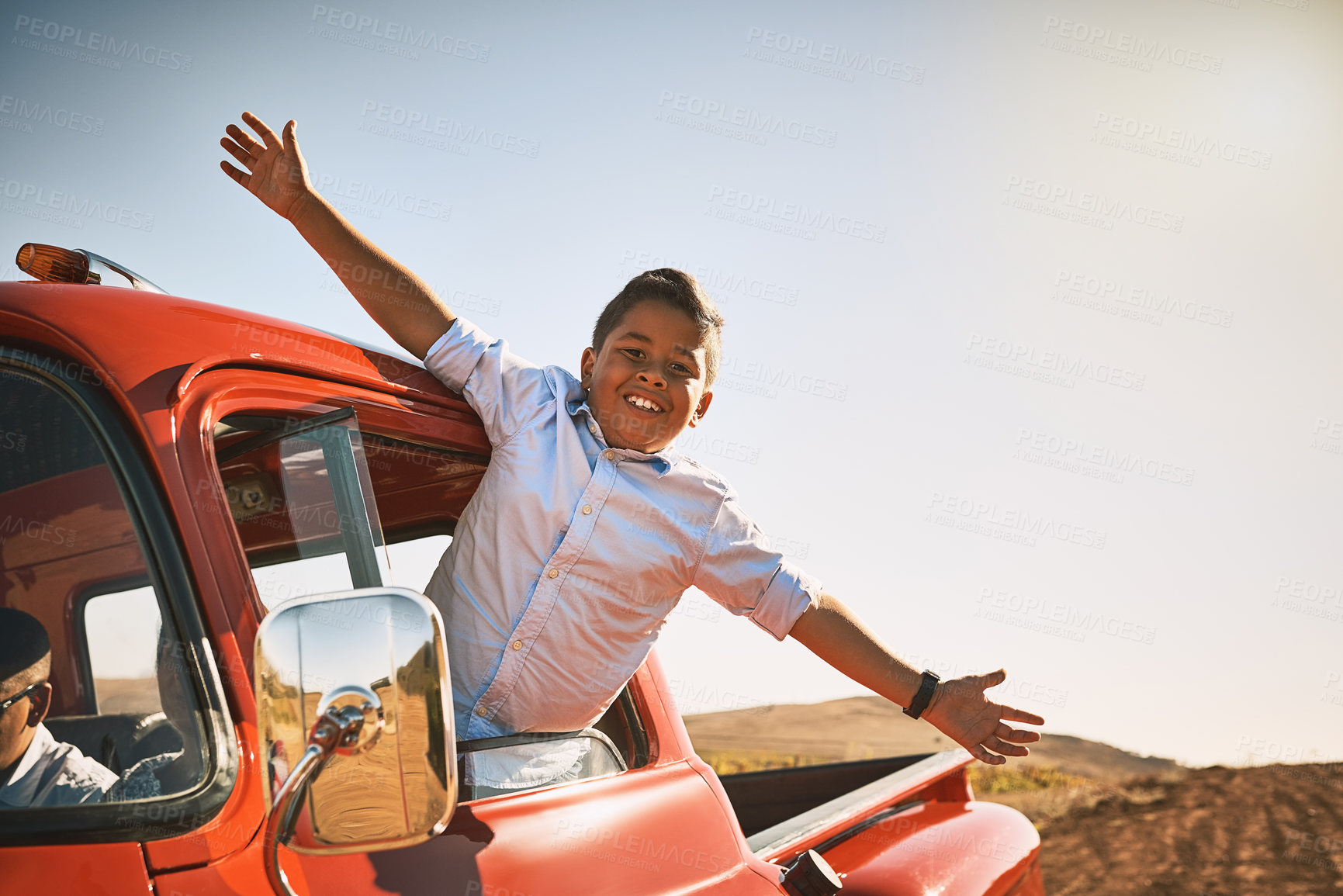 Buy stock photo Shot of a young cheerful boy leaning out of a red pickup truck with his arms stretched out while looking into the camera
