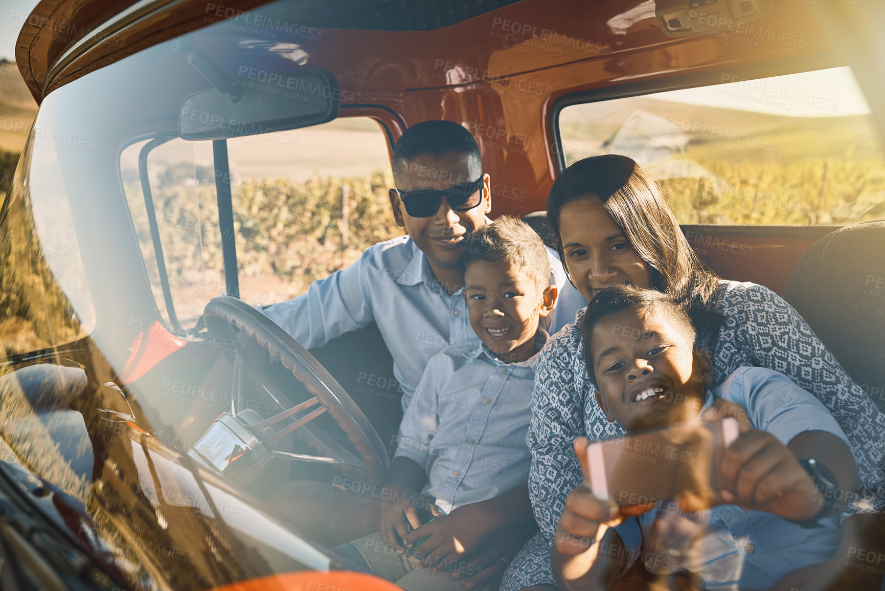 Buy stock photo Shot of a cheerful young family driving in a red pickup truck on a rural road while taking a self portrait on a cellphone together
