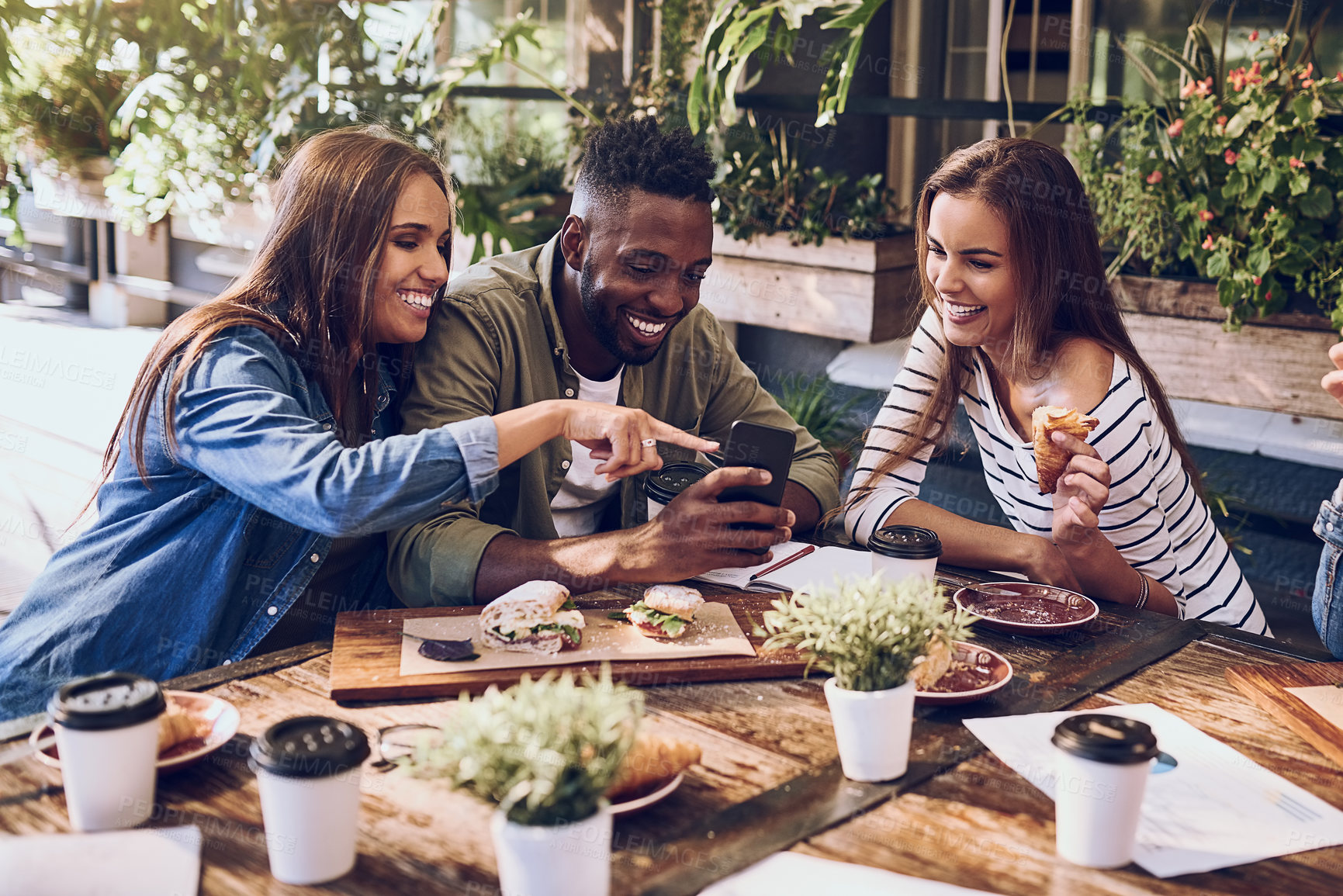 Buy stock photo Shot of three friends looking at something on a cellphone while out for lunch