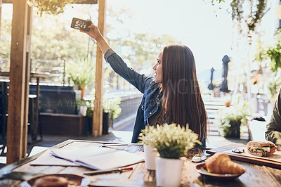 Buy stock photo Shot of a young woman taking a selfie while out with friends at a cafe
