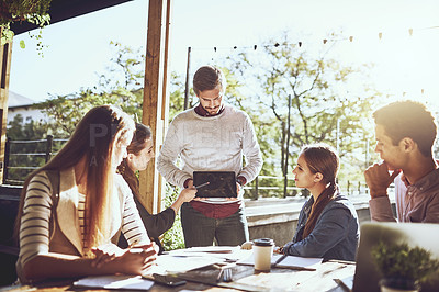 Buy stock photo Shot of a team of colleagues using a digital tablet together during a meeting at an outdoor cafe