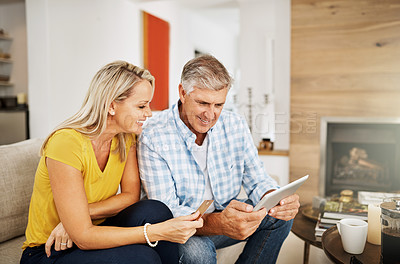 Buy stock photo Beautiful, smiling mature couple buying online, shopping on their digital tablet together on their home living room sofa. Husband making financial payments through internet banking with his wife