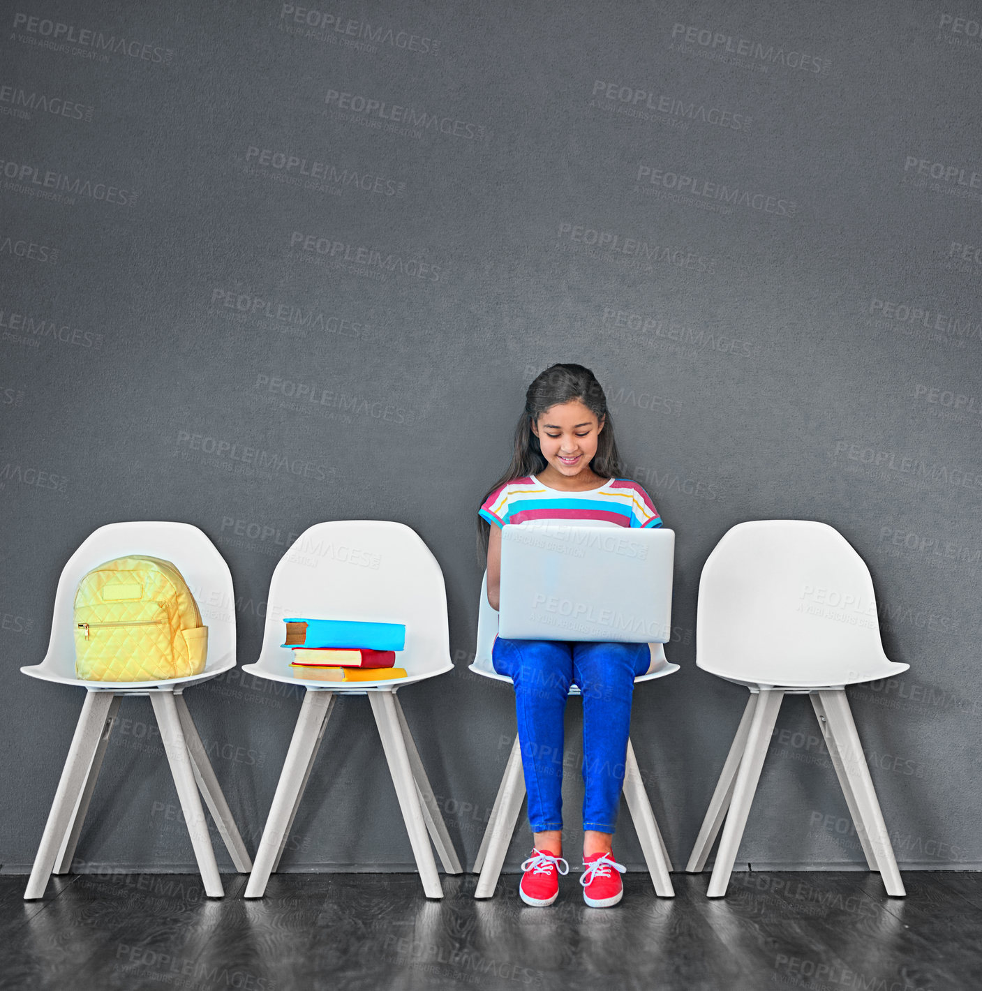 Buy stock photo Child, chair and laptop for learning and education while typing for research on internet. Happy girl kid or student against a grey wall with technology, book and backpack in a waiting room with space