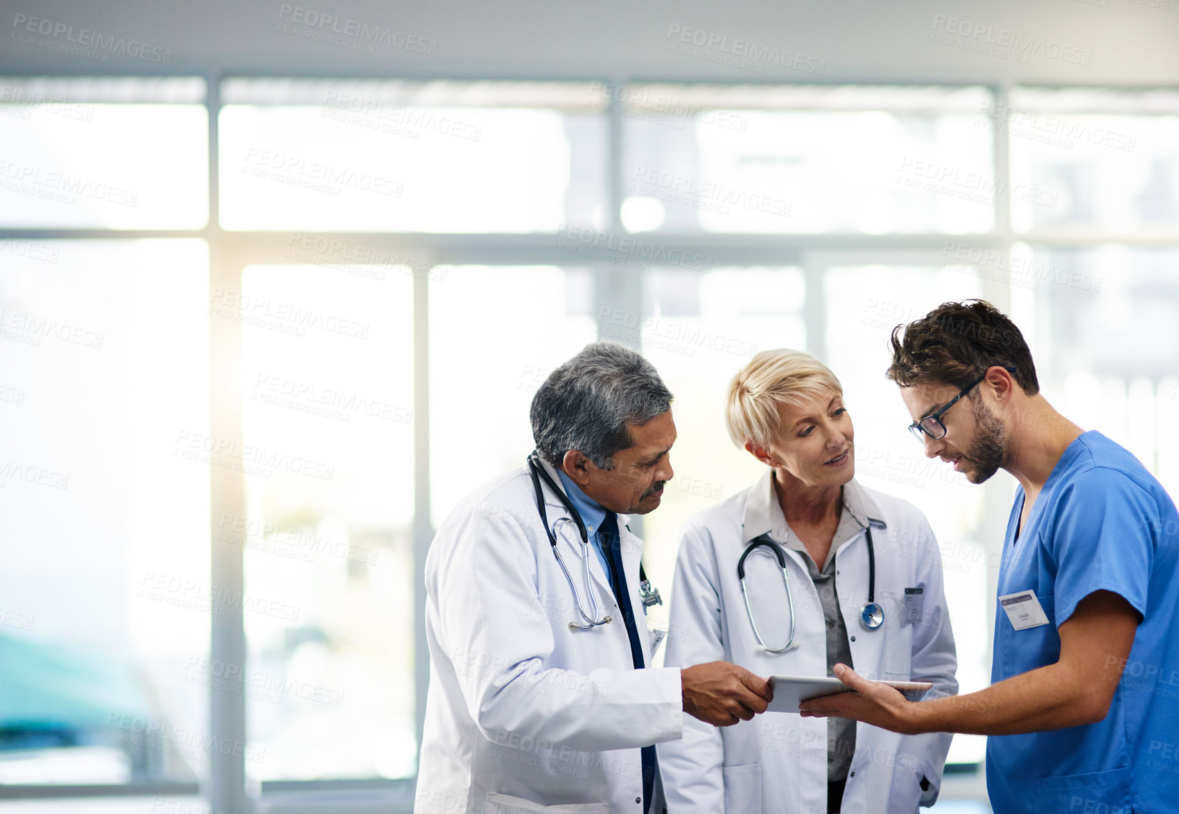 Buy stock photo Medical professional, team and workers holding tablet, talking and solving a problem together online while standing at work in a hospital. Health experts discussing, planning and doing research