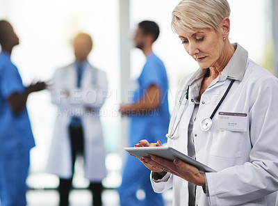 Buy stock photo Shot of a mature doctor using a digital tablet with her colleagues in the background