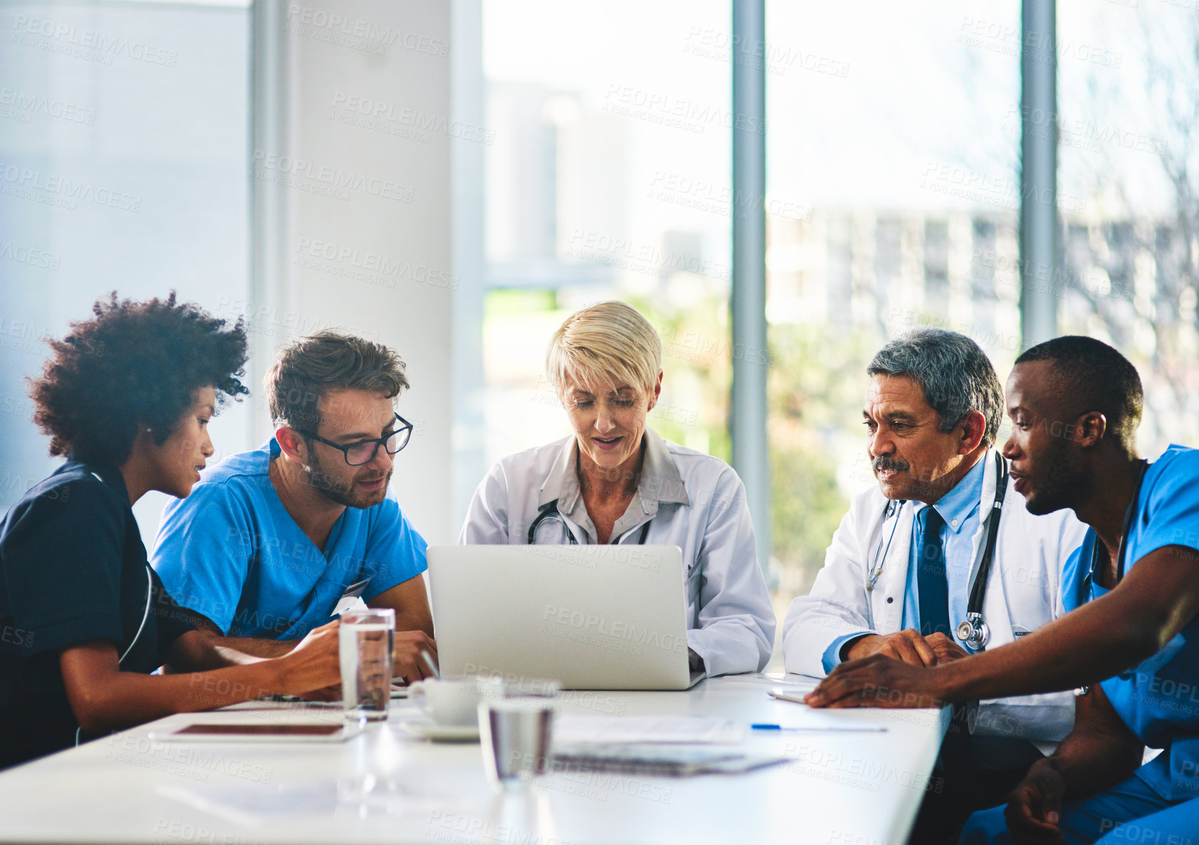 Buy stock photo Team of doctors in a meeting planning and brainstorming in a boardroom using a laptop to read notes. Group of healthcare professionals discussing and talking in a modern office