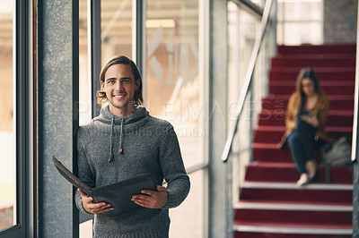Buy stock photo Cropped portrait of a handsome young university student studying while standing in a hallway on campus