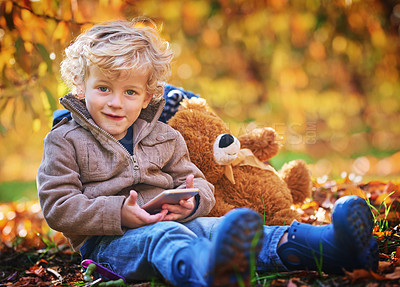Buy stock photo Cropped portrait of an adorable little boy using his cellphone while sitting outdoors during autumn