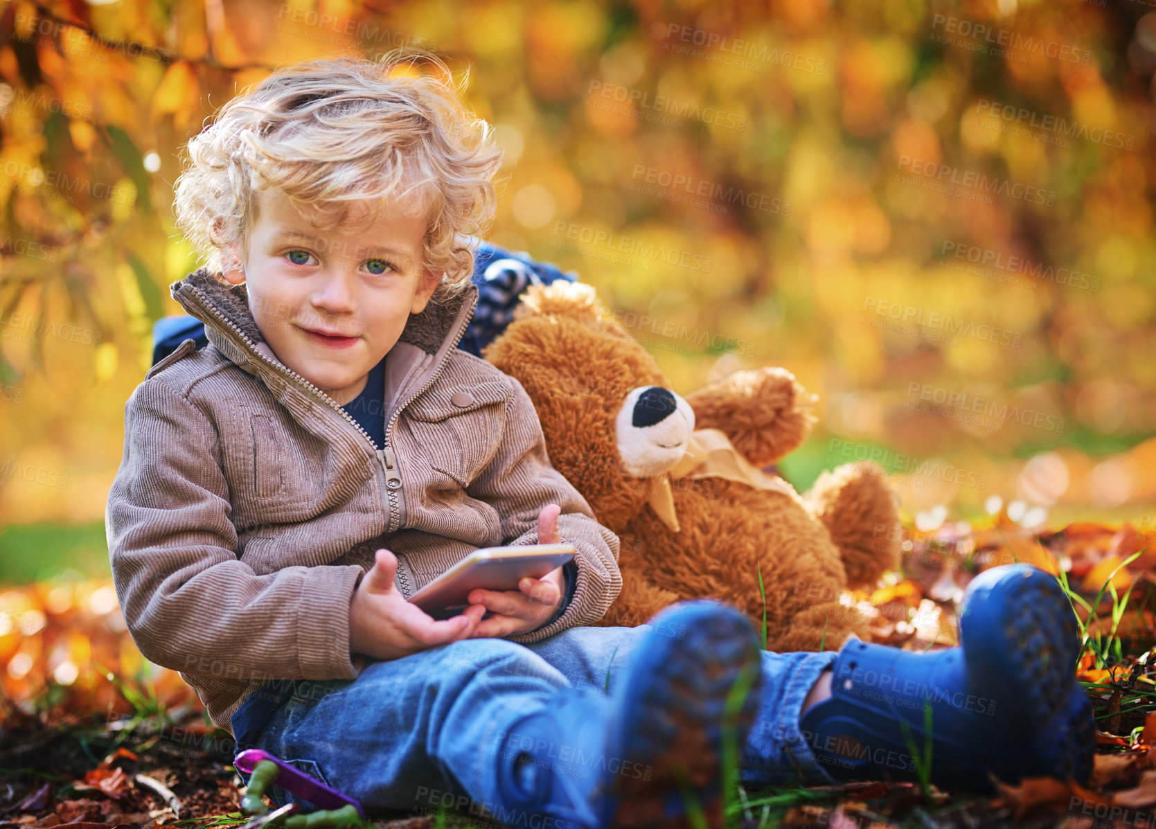 Buy stock photo Cropped portrait of an adorable little boy using his cellphone while sitting outdoors during autumn