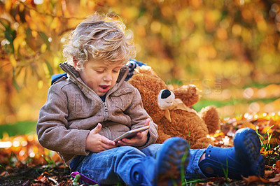 Buy stock photo Cropped shot of an adorable little boy using his cellphone while sitting outdoors during autumn