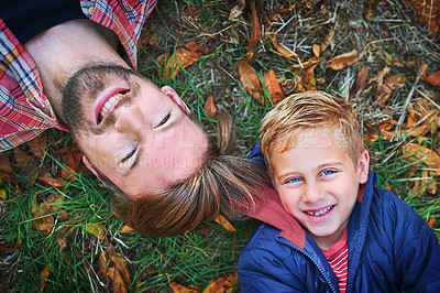 Buy stock photo High angle portrait of a handsome young man and his son lying on the grass outside during autumn