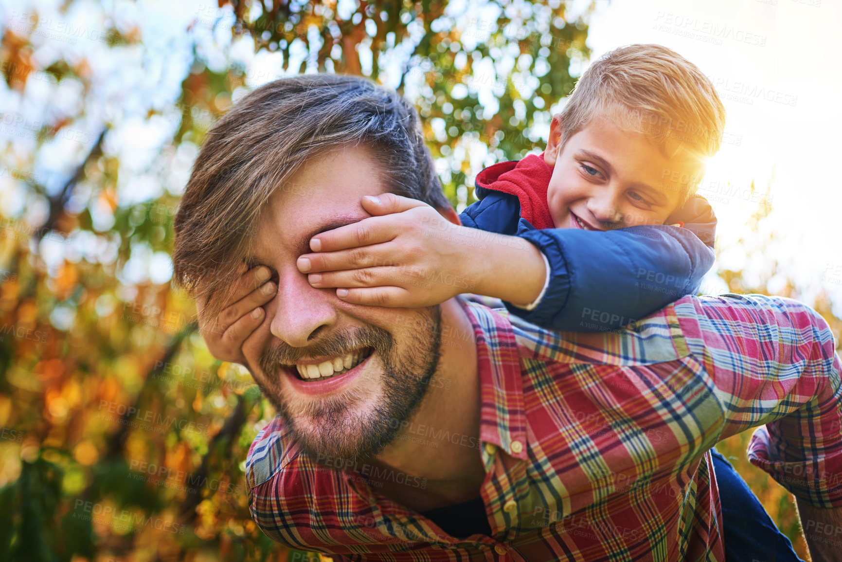 Buy stock photo Cropped shot of an adorable young boy closing his father's eyes while being piggybacked outside during autumn